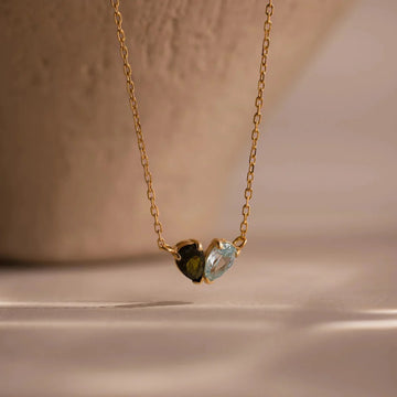 Gold necklace with two heart-shaped gemstones on a beige background