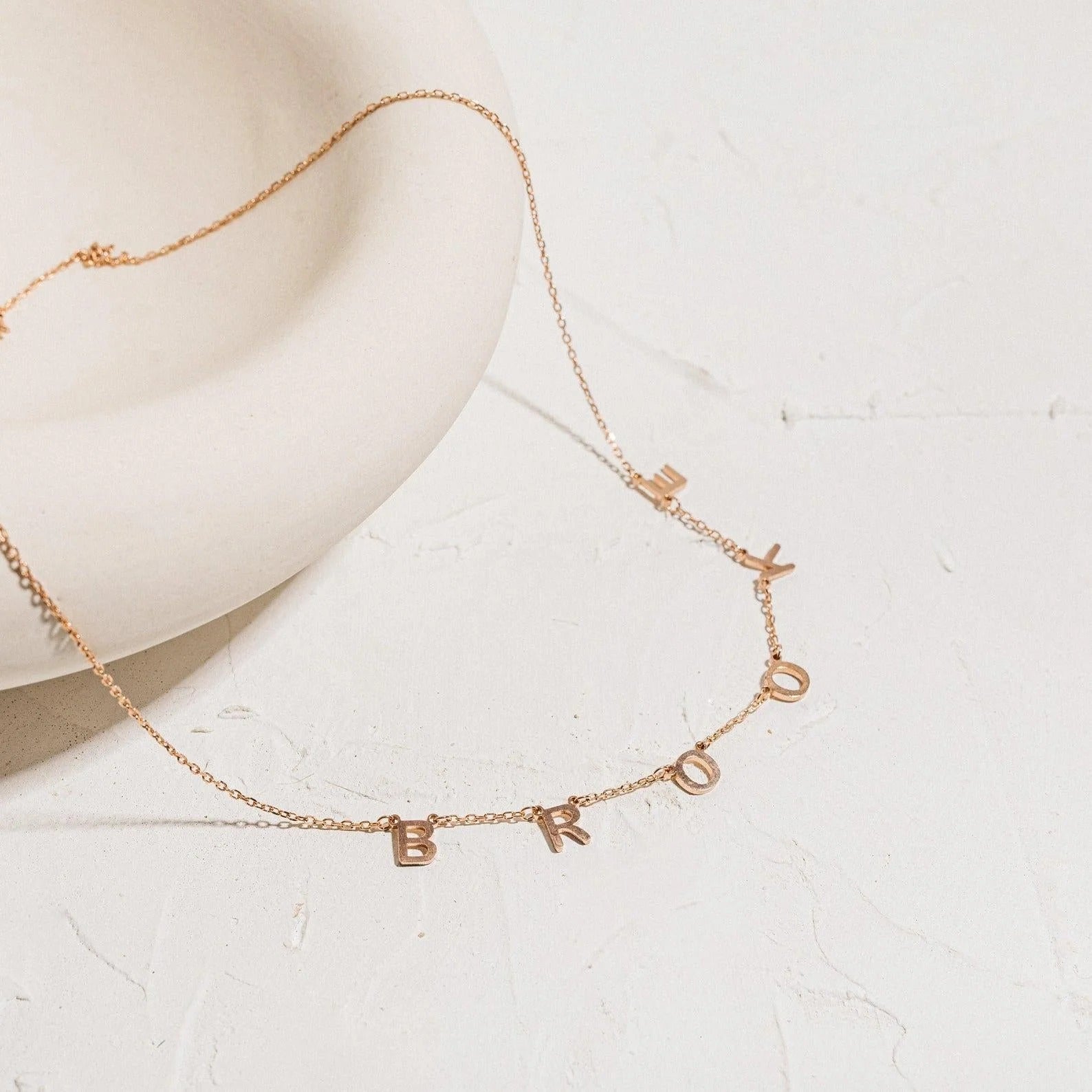 Rose gold necklace with letter charms on a light background
