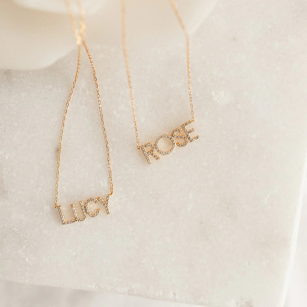 Two gold name necklaces on a soft white background