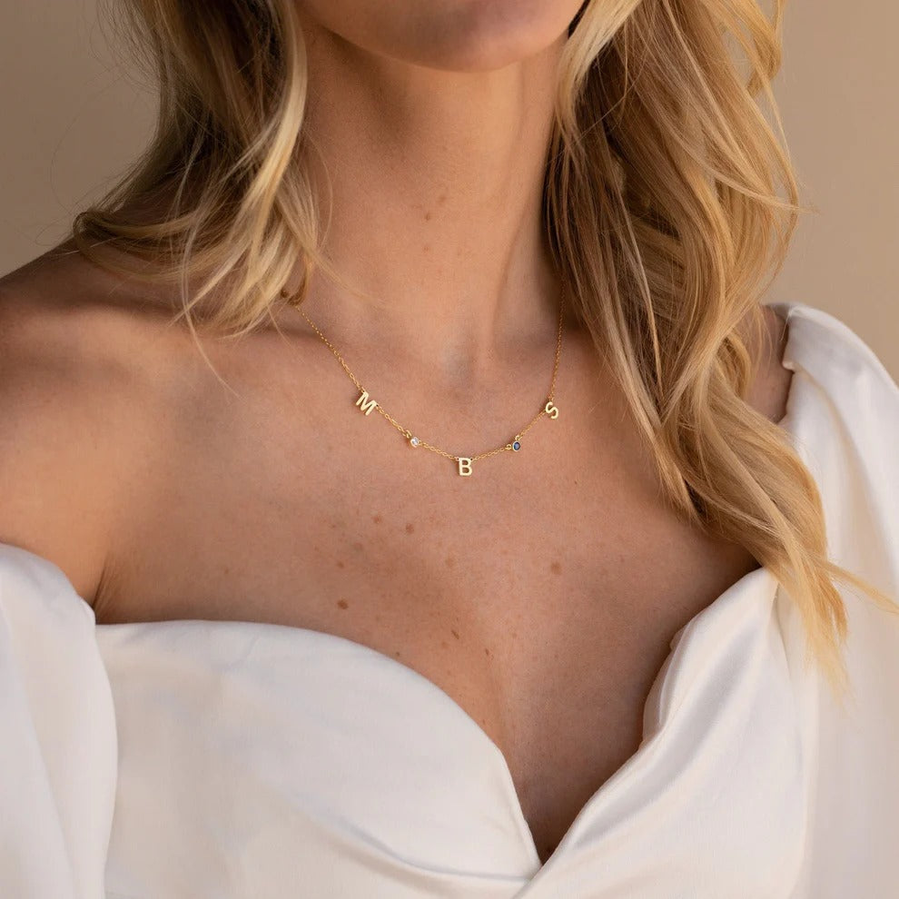 Necklace with letter beads worn by a person with blonde hair and a white garment.