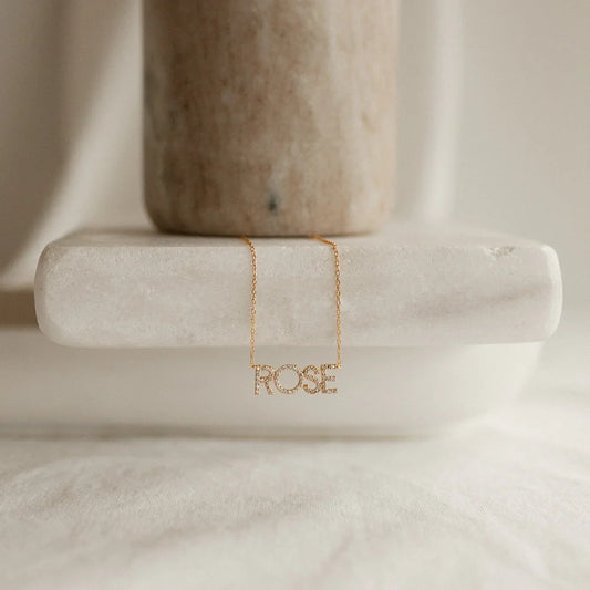 Gold necklace with 'ROSE' pendant on a marble surface