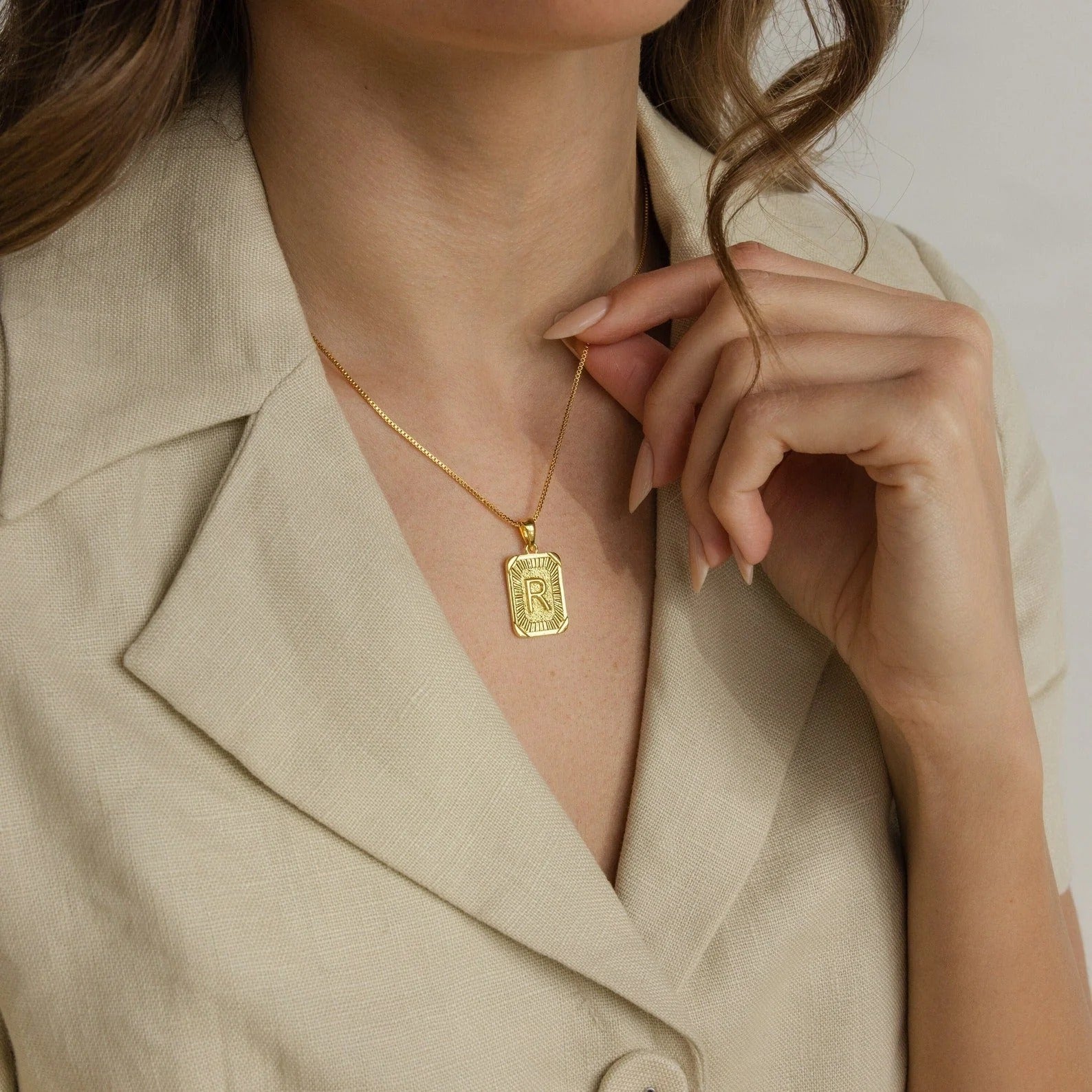Gold necklace with a pendant worn by a person in a beige outfit.