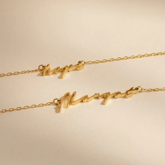Two gold necklaces with script designs on a beige background