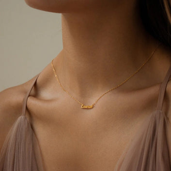 Gold necklace with 'Lauren' pendant on a person wearing a beige top against a neutral background