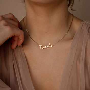 Gold necklace with 'Natalie' on a person wearing a sheer beige garment.