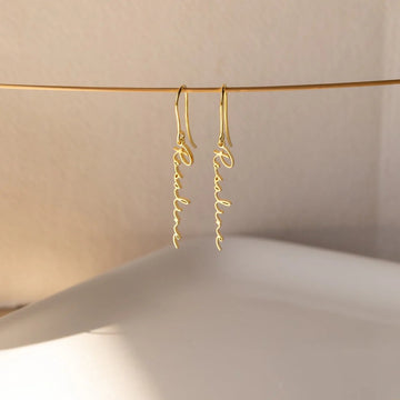 Gold earrings with 'Romantic' inscription hanging against a neutral background