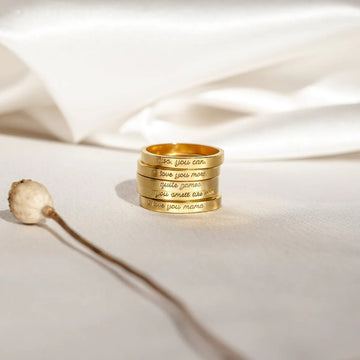 Stack of gold rings with engraved text on a white fabric background