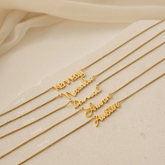 Gold name necklaces on a beige surface