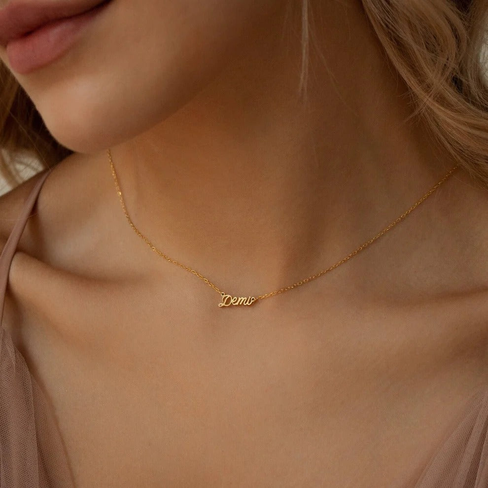 Gold necklace with 'Demi' pendant on a person wearing a beige top.