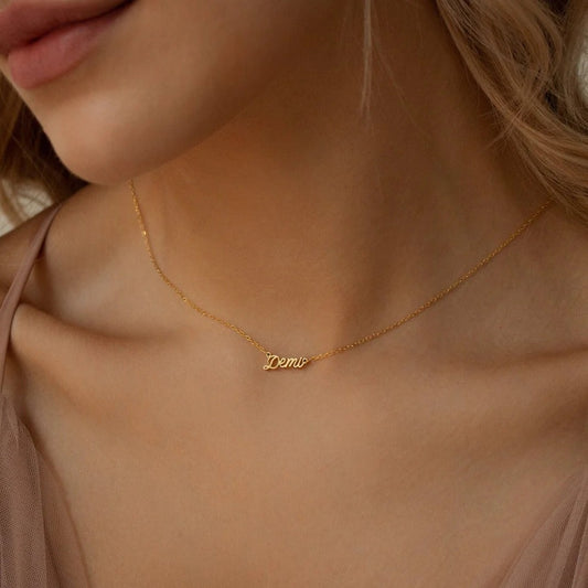 Gold necklace with 'Demi' pendant on a person wearing a beige top.