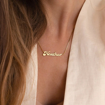 Gold necklace with 'Heather' pendant on a person wearing a beige top.