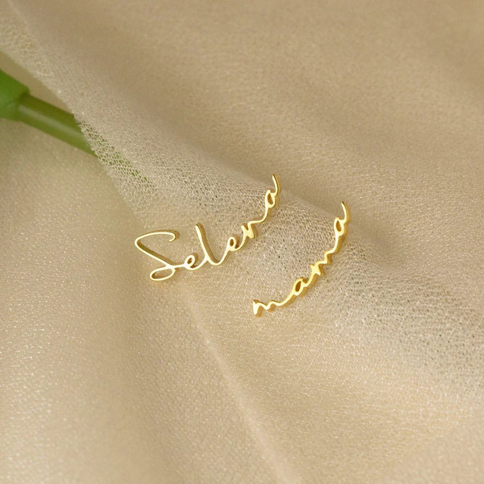 Gold hoop earrings with 'Selen' engraving on a beige fabric background