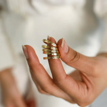 Hand wearing multiple gold rings with a blurred background