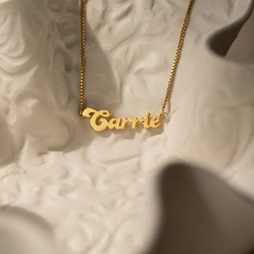 Gold 'Carrie' necklace on a textured beige surface