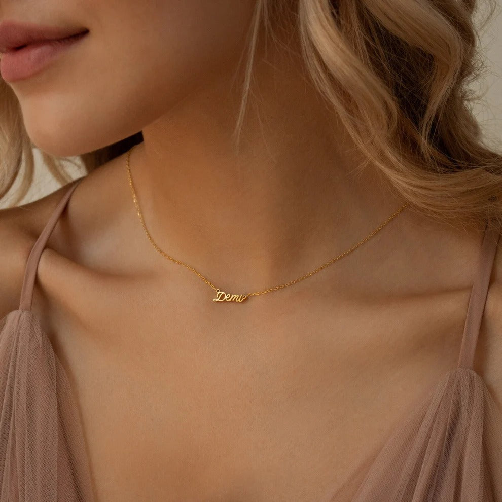 Gold necklace with 'Demi' pendant on a model wearing a beige top.
