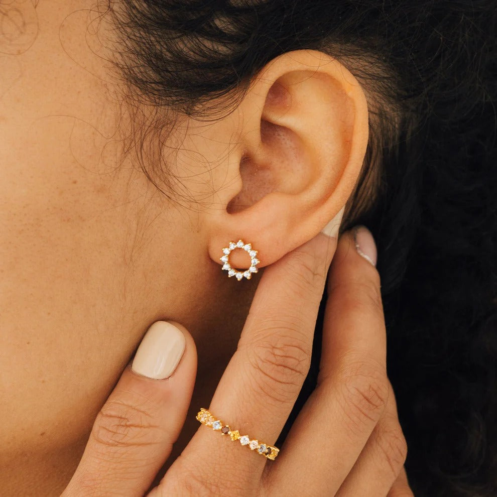 Close-up of an ear wearing a gold hoop earring with a hand adjusting it.