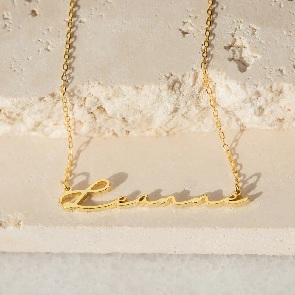 Gold necklace with 'Lana' pendant on a light stone background