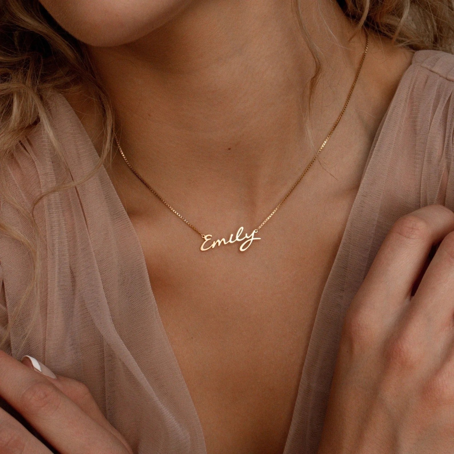 Gold necklace with 'Emily' pendant on a person wearing a sheer top.