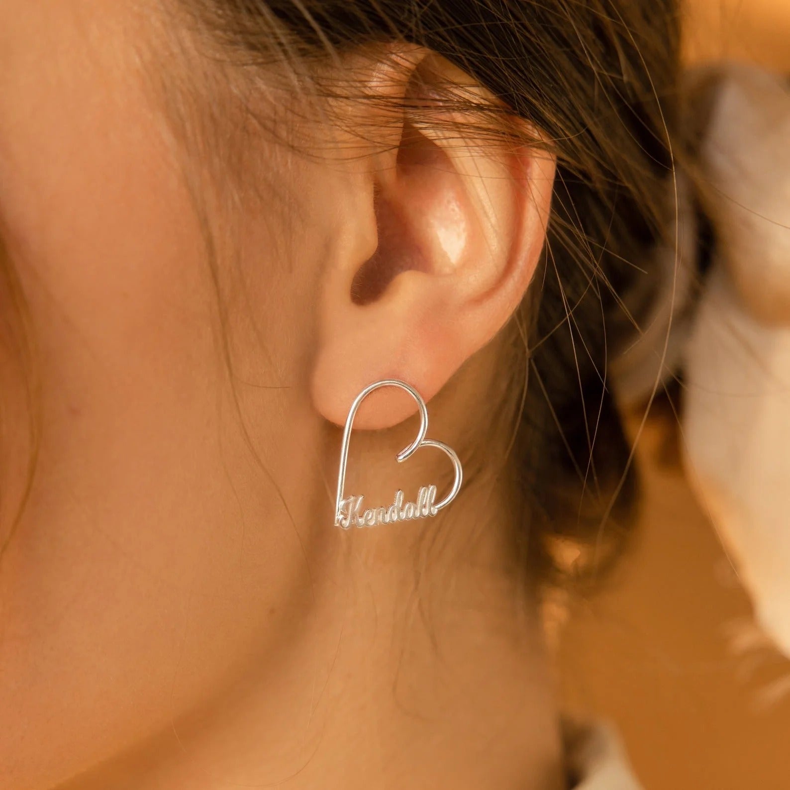 Heart-shaped earring with engraved text worn by a person.