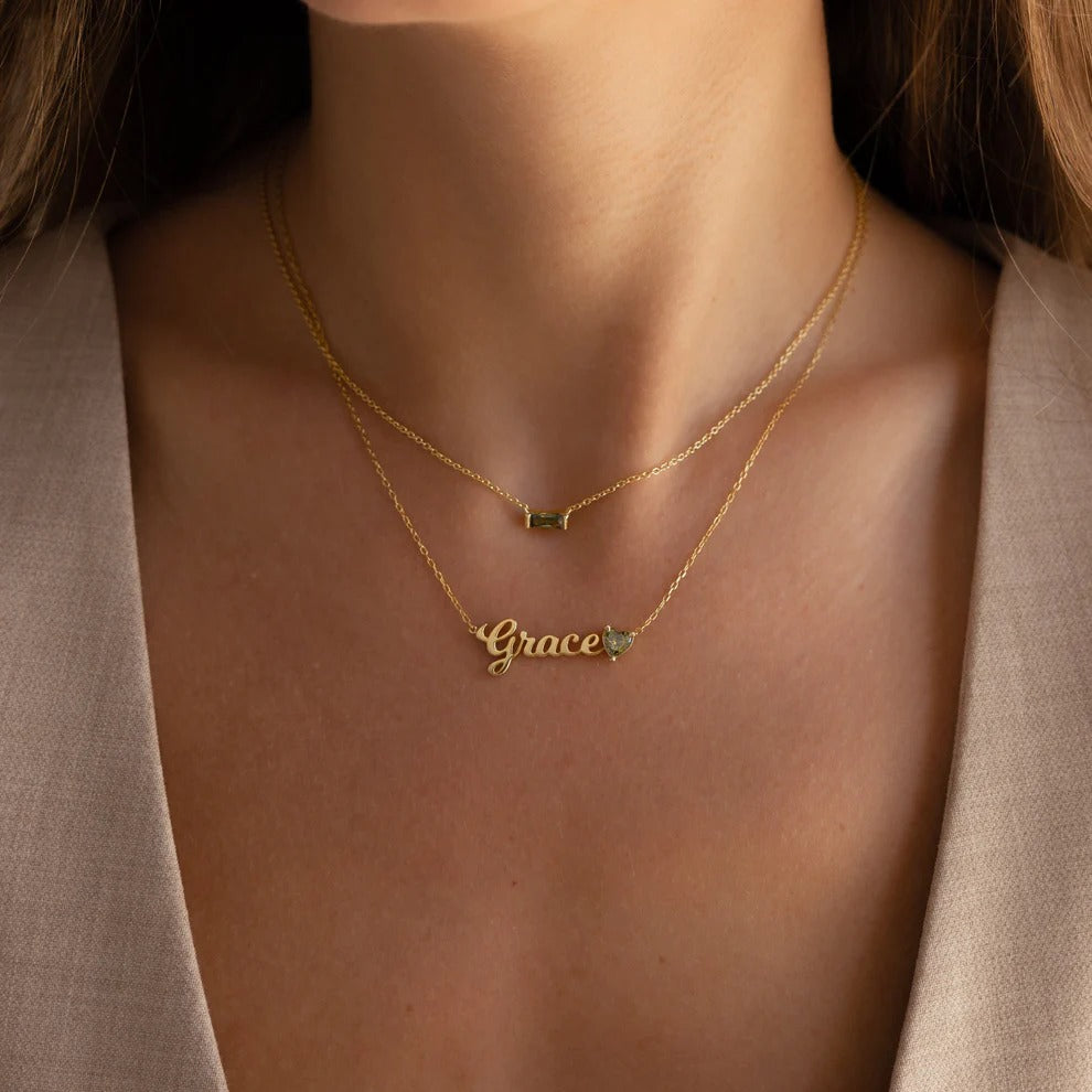 Gold necklace with 'Grace' pendant on a person wearing a beige cardigan.