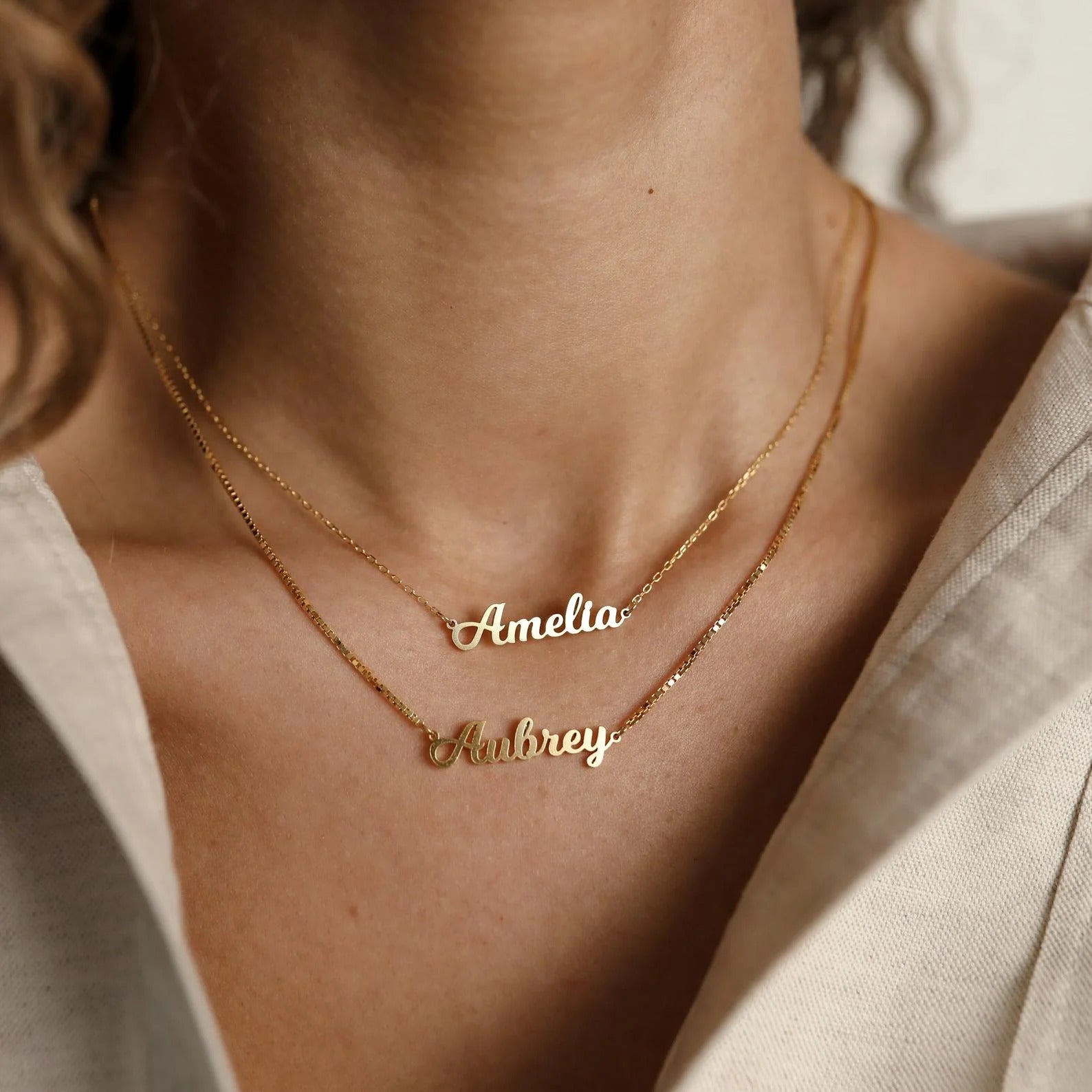 Gold name necklaces on a person wearing a beige top.