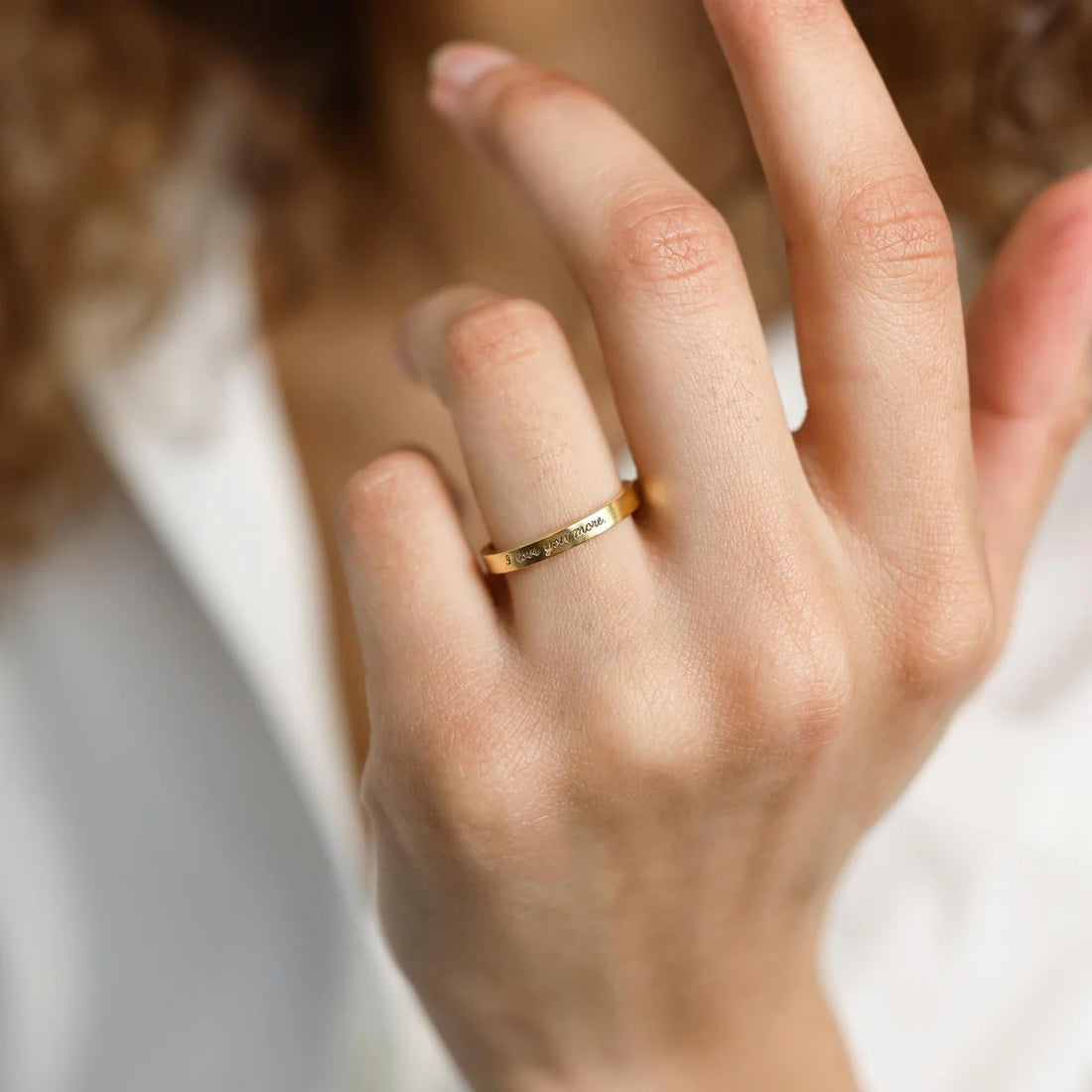 Close-up of a hand wearing a gold ring with engraved text on a blurred background