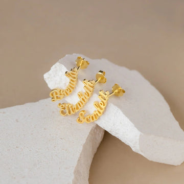 Gold hoop earrings with 'Moments' text on a beige stone surface