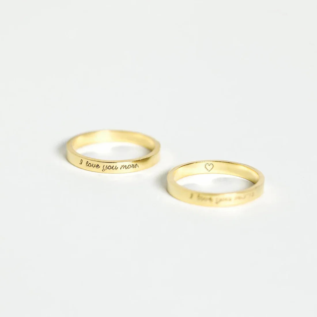 Two gold rings with engraved text on a white background