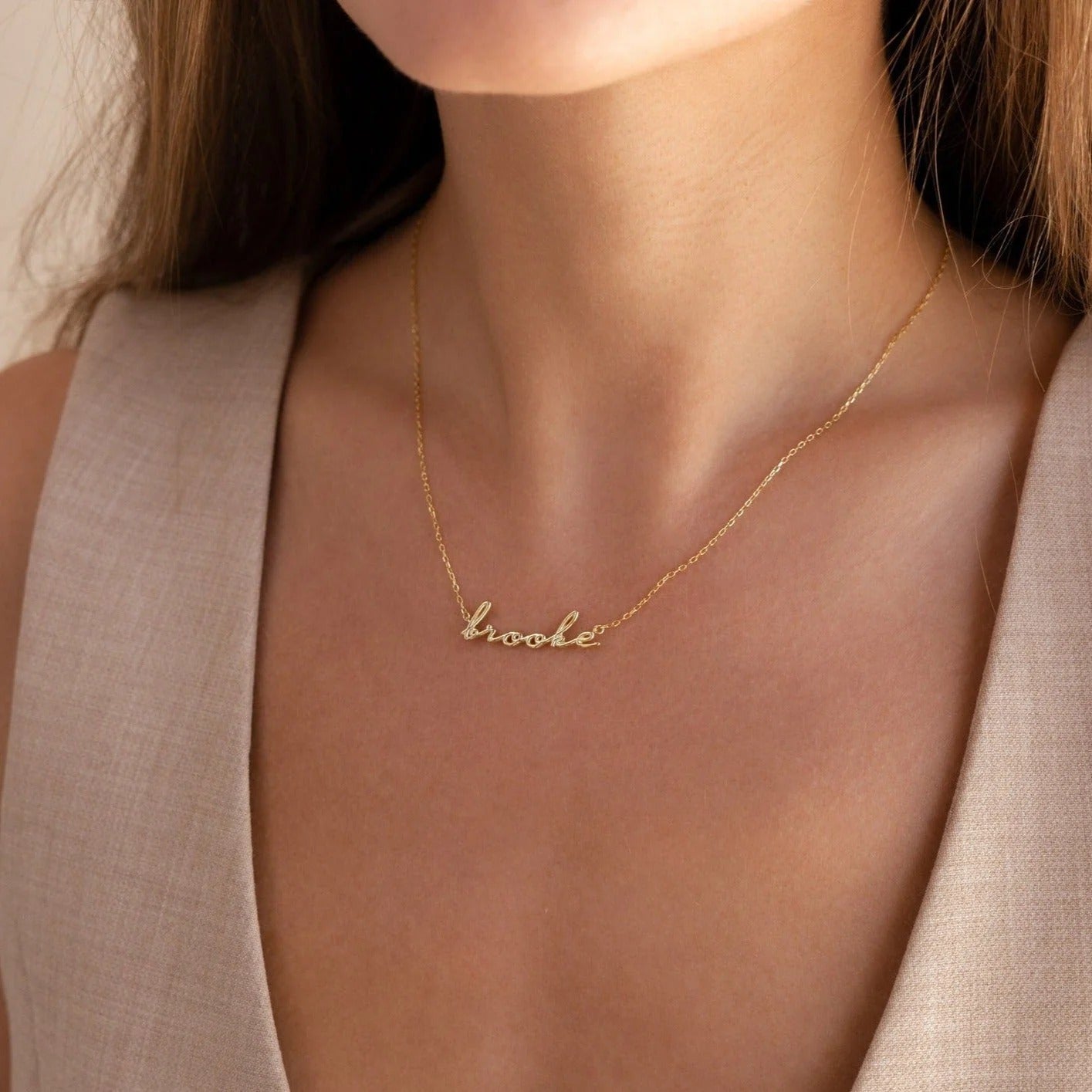 Gold necklace with 'book' pendant on a person wearing a beige top.
