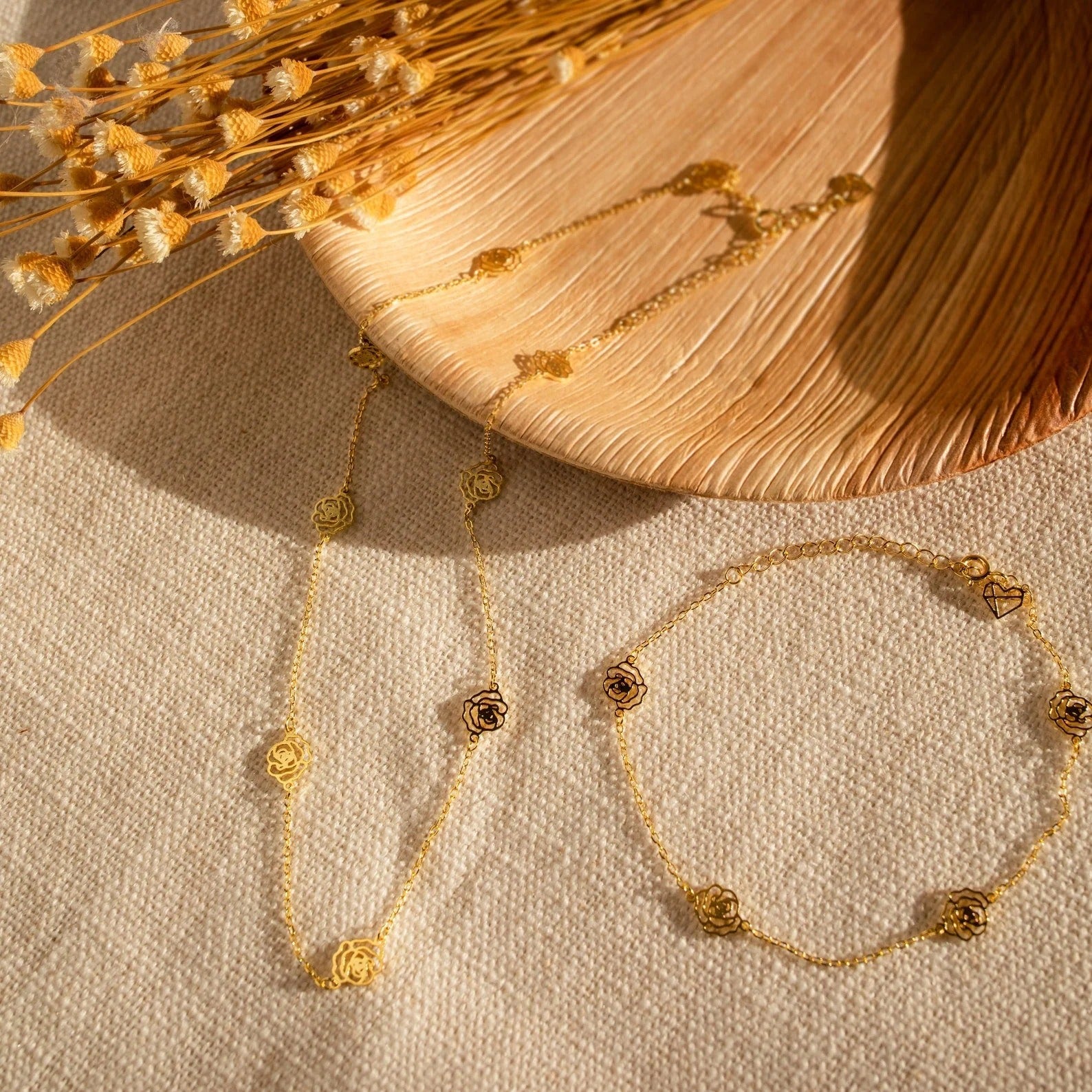Gold necklace and bracelet on a textured surface with dried flowers.