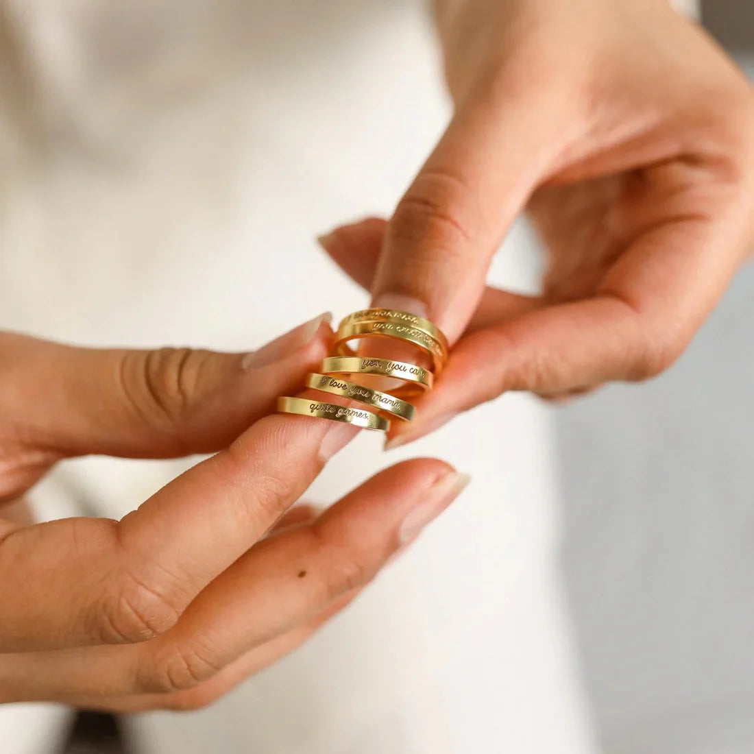 Gold rings being held between two hands with a neutral background