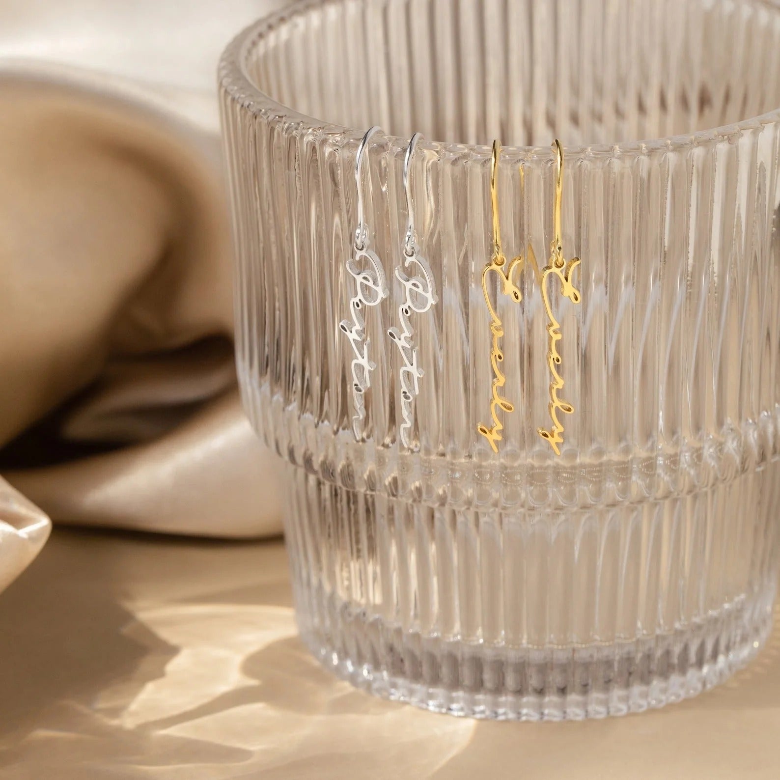 Gold and silver earrings in a clear glass container on a beige surface