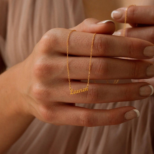 Gold necklace with 'Lauren' engraved on a hand against a neutral background