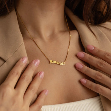 Gold necklace with 'Amanda' nameplate worn by a person, with hands gently touching the chest.