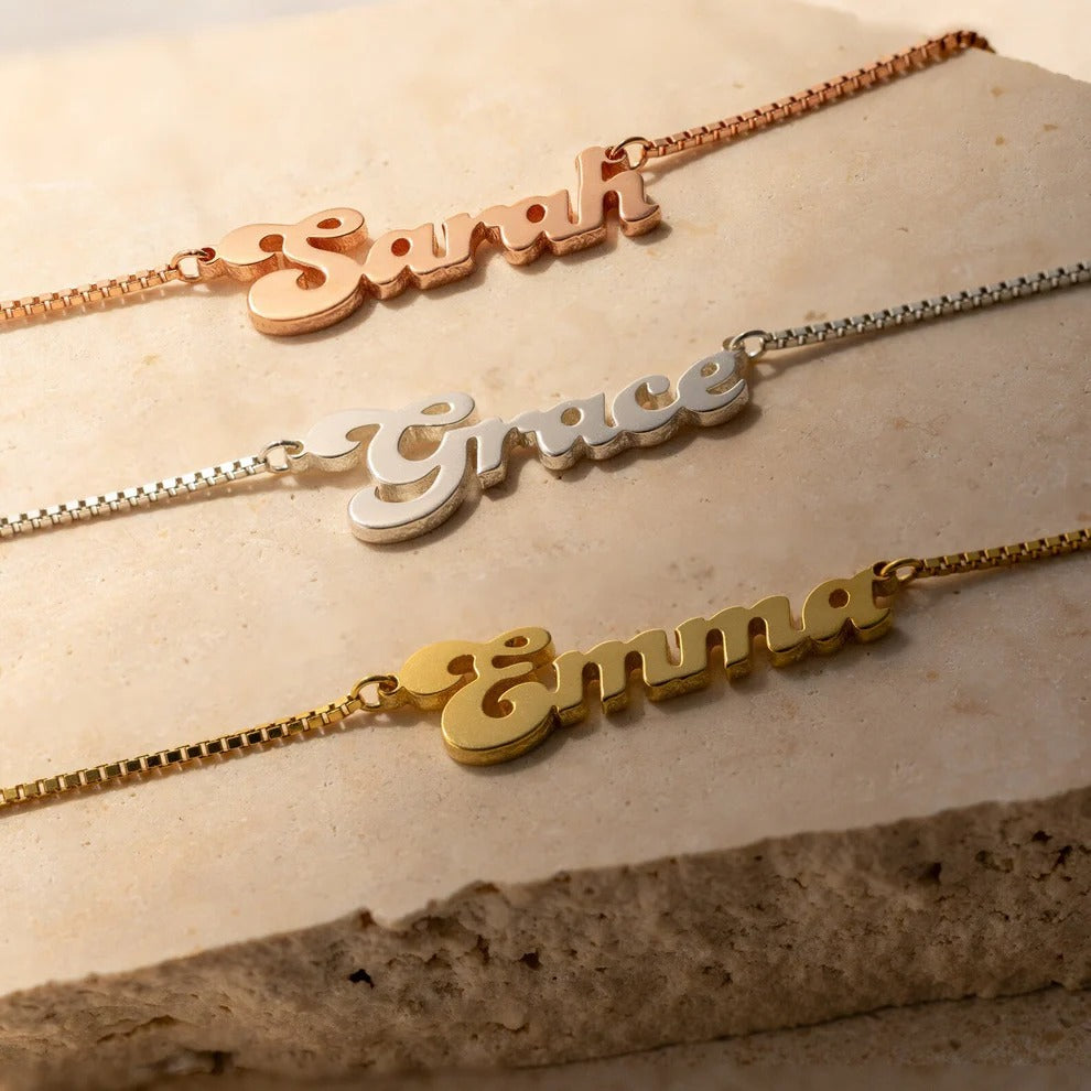 Three name necklaces on a textured surface, each with a different name.