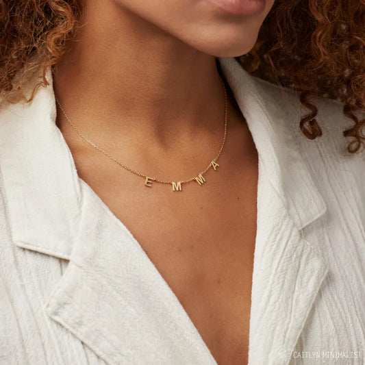 Gold necklace with 'EMMA' letters worn by a person in a white shirt.