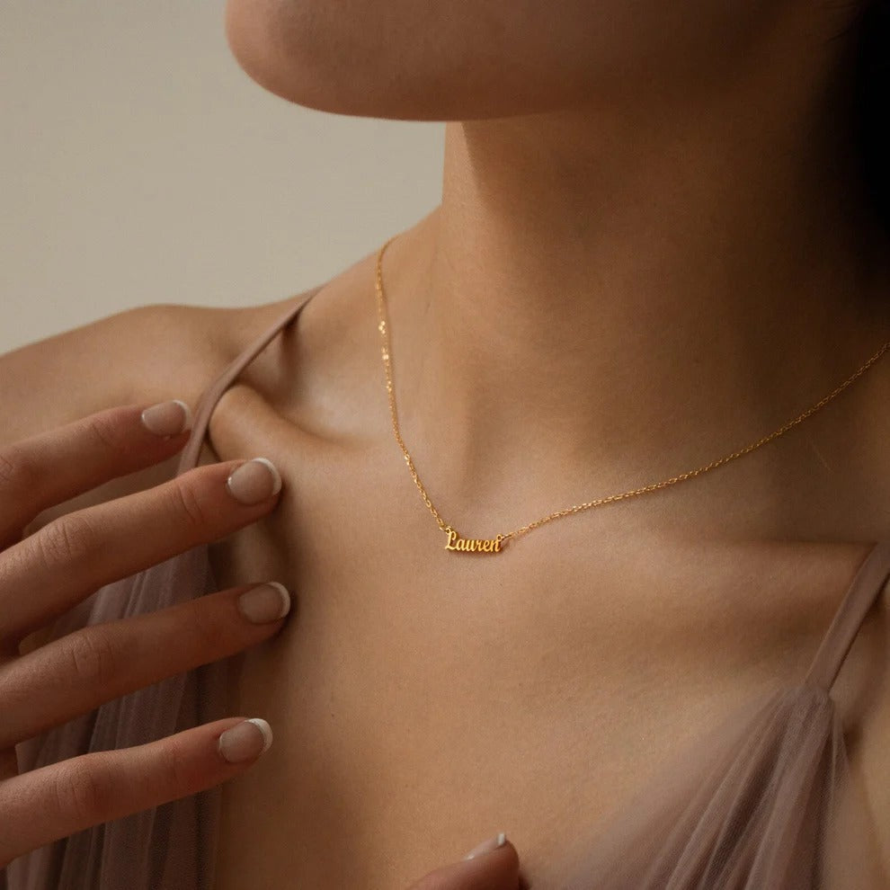 Gold necklace with name pendant worn by a person, against a neutral background