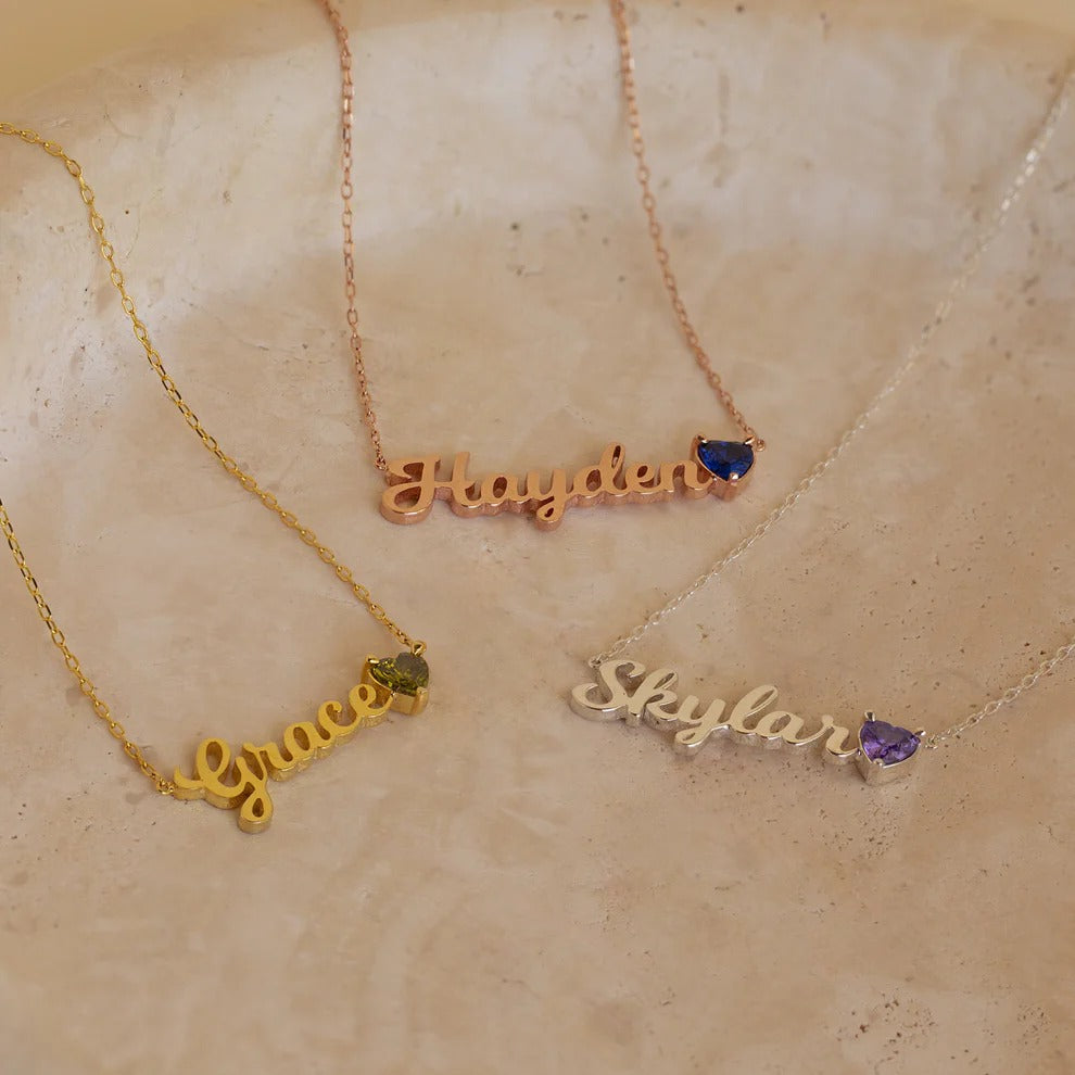 Three name necklaces with gemstones on a beige stone surface