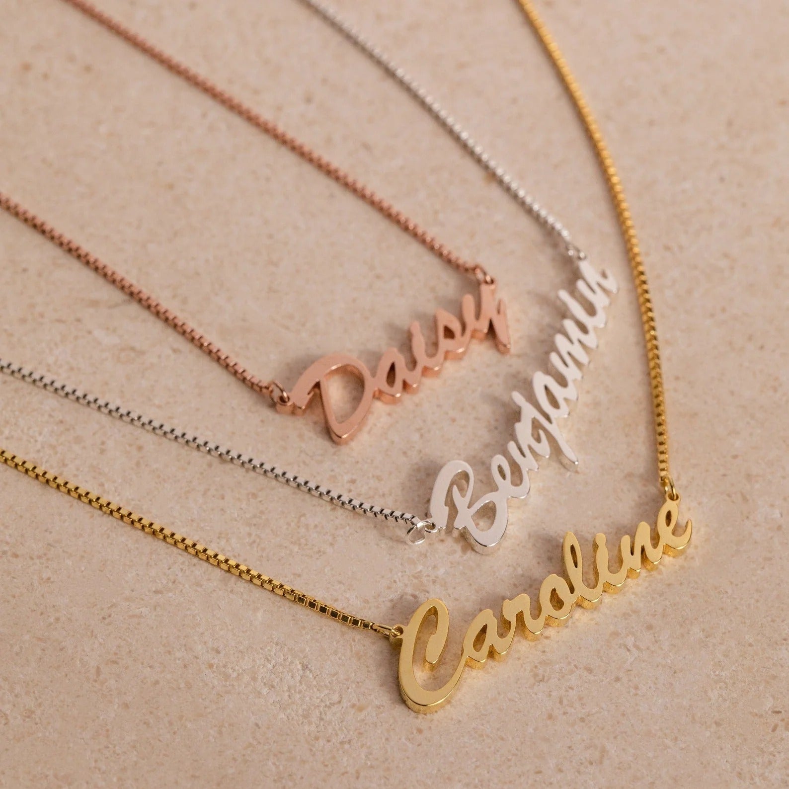 Three name necklaces in gold, rose gold, and silver on a beige background