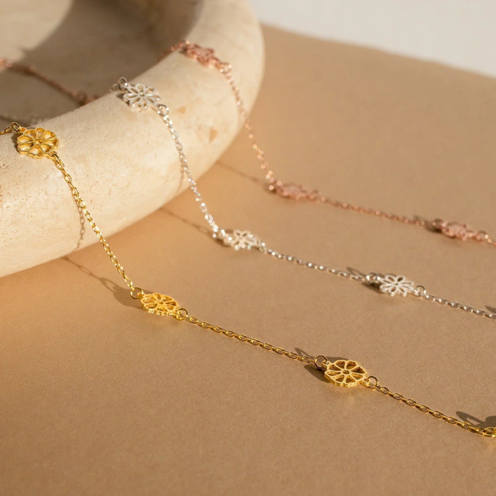 Three gold and silver necklaces on a beige surface