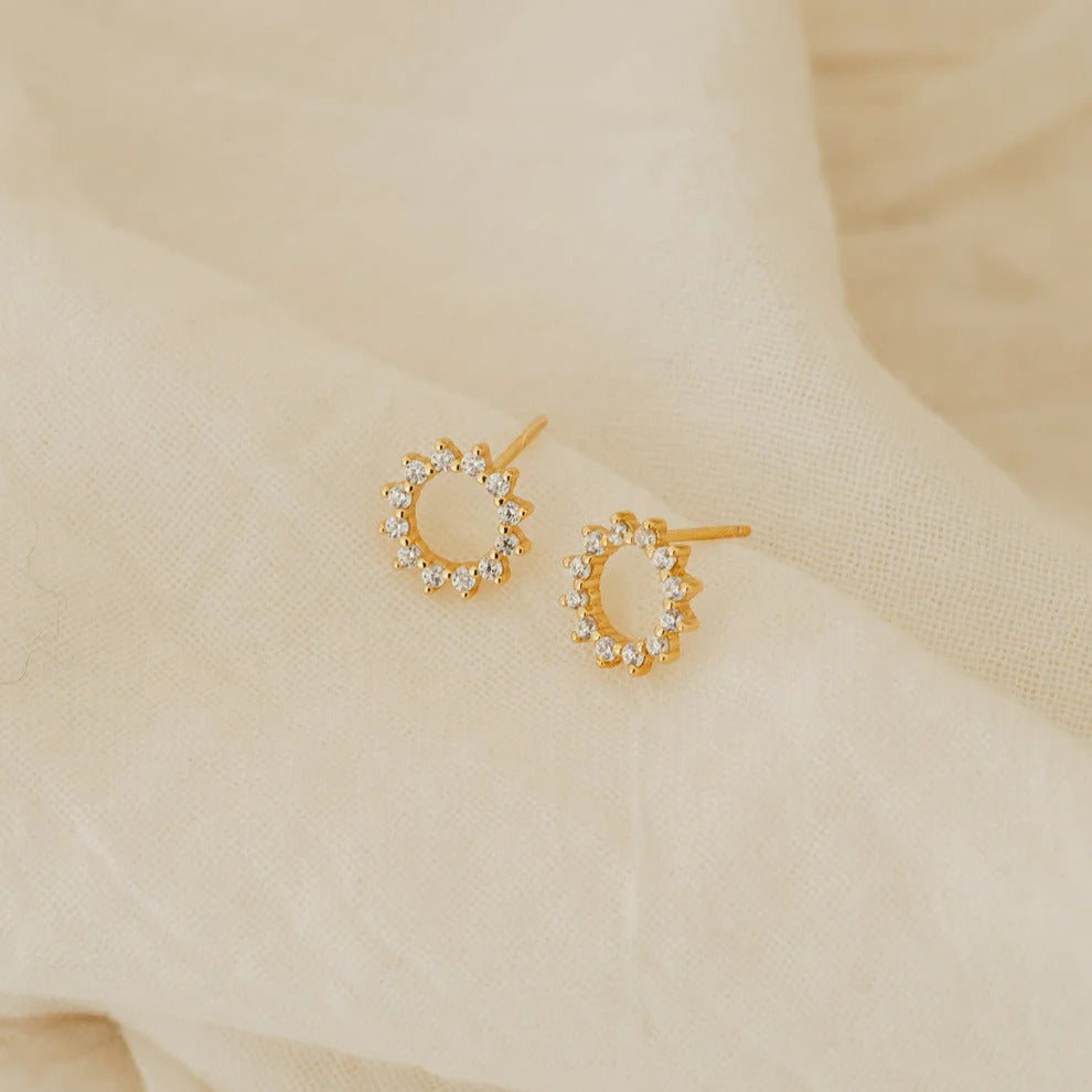 Gold hoop earrings with small diamonds on a beige fabric background