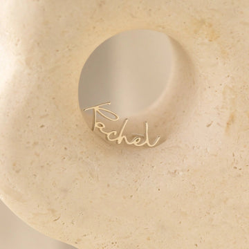 Gold ring with 'Rachel' engraving on a beige stone surface