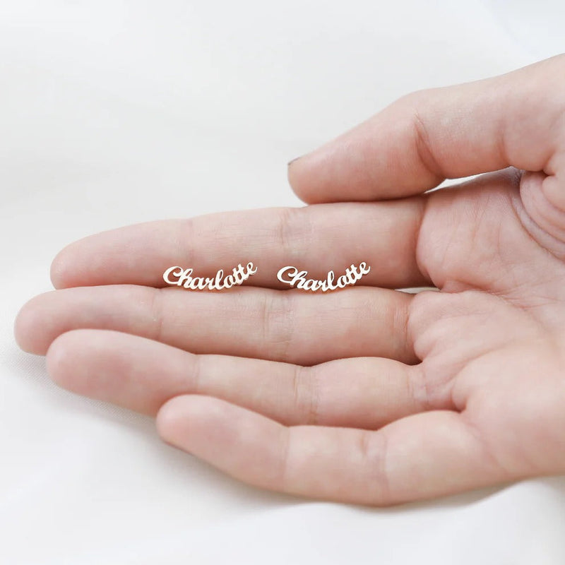 Gold 'Charlotte' earrings held in a hand on a white background