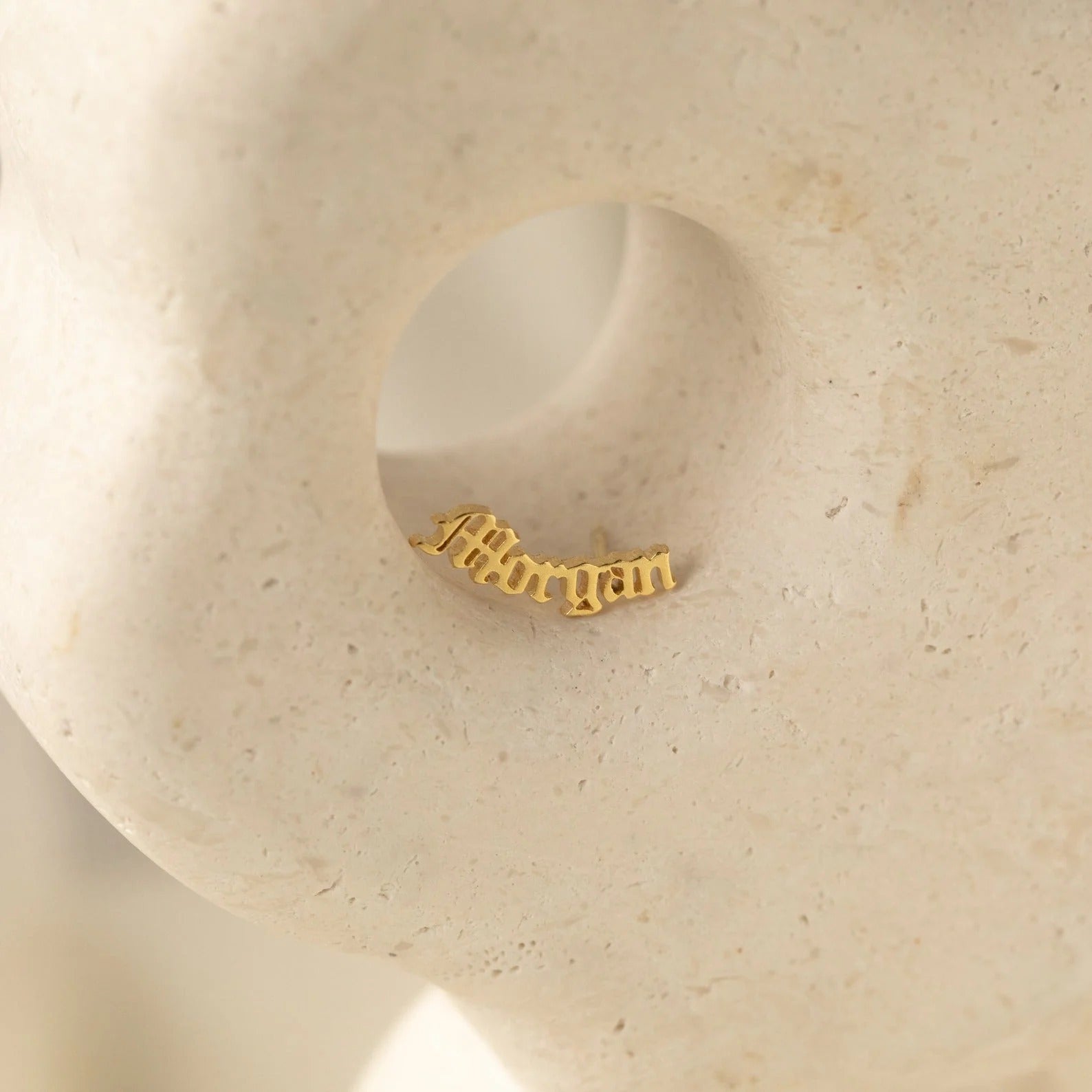 Gold nameplate earring on a beige stone surface
