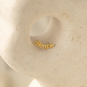 Gold nameplate earring on a beige stone surface