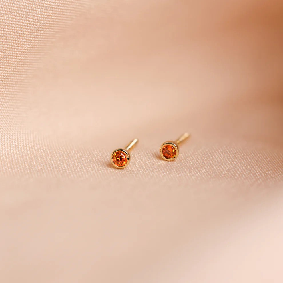 Pair of gold earrings with orange gemstones on a beige fabric background