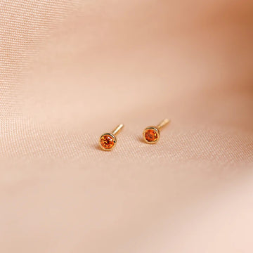 Pair of gold earrings with orange gemstones on a beige fabric background