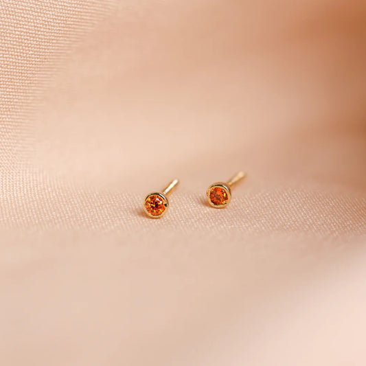 Pair of gold earrings with orange gemstones on a beige fabric background