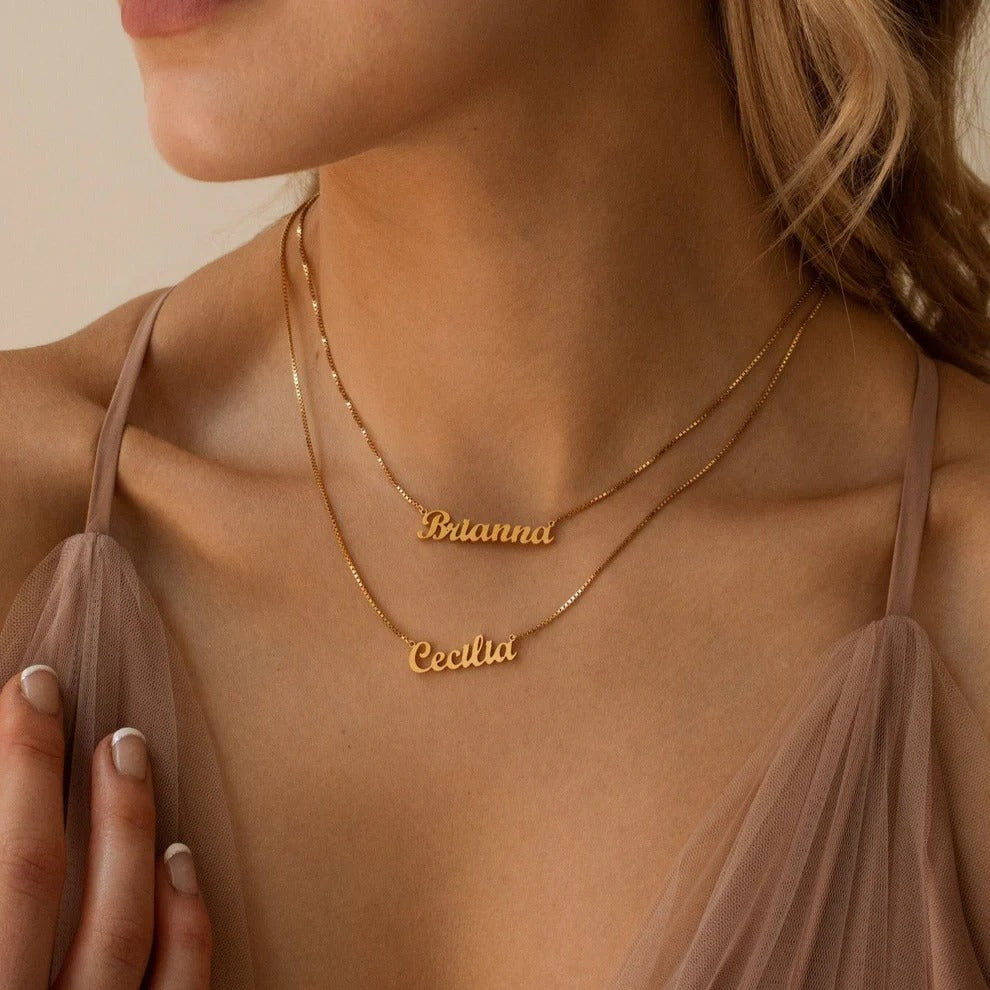 Gold name necklaces on a person wearing a sheer top.