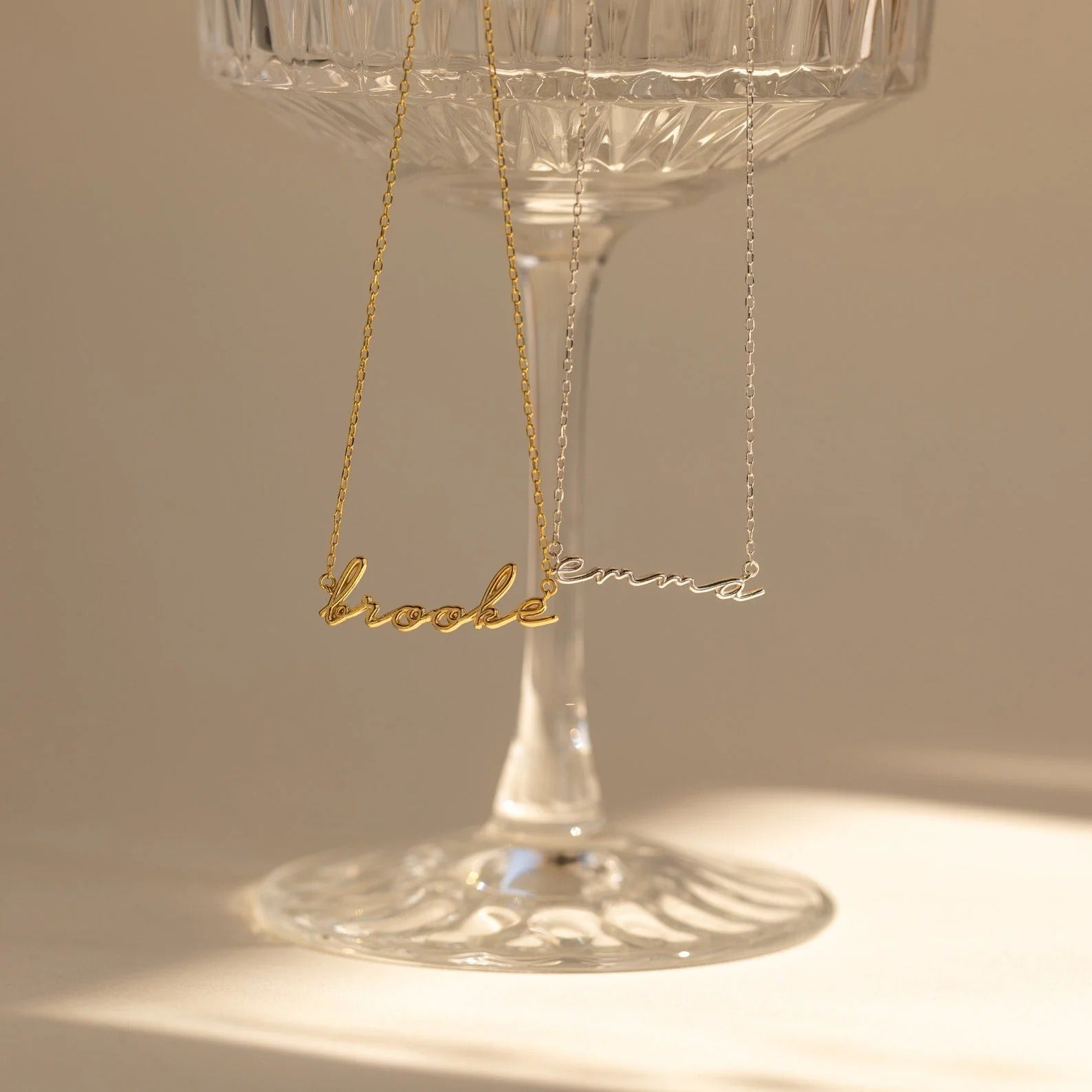Gold name necklace on a glass stand with a warm glow